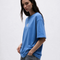 A woman wearing a blue olono oversized short-sleeve t-shirt with a small white graphic on the left chest, paired with gray jeans, against a plain light gray background.
