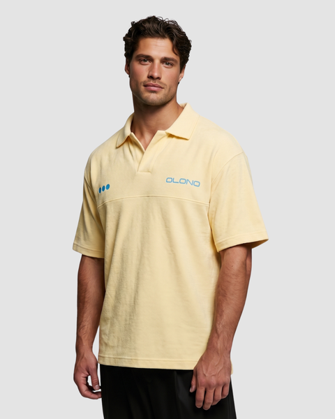 Man wearing a yellow polo shirt with a brand logo on a plain background