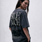 A woman wearing a dark charcoal gray oversized graphic T-shirt, shown from the back. The shirt features the word 'SILENCE' in large, stylized white letters with a black distressed graphic underneath and small white text near the hem.